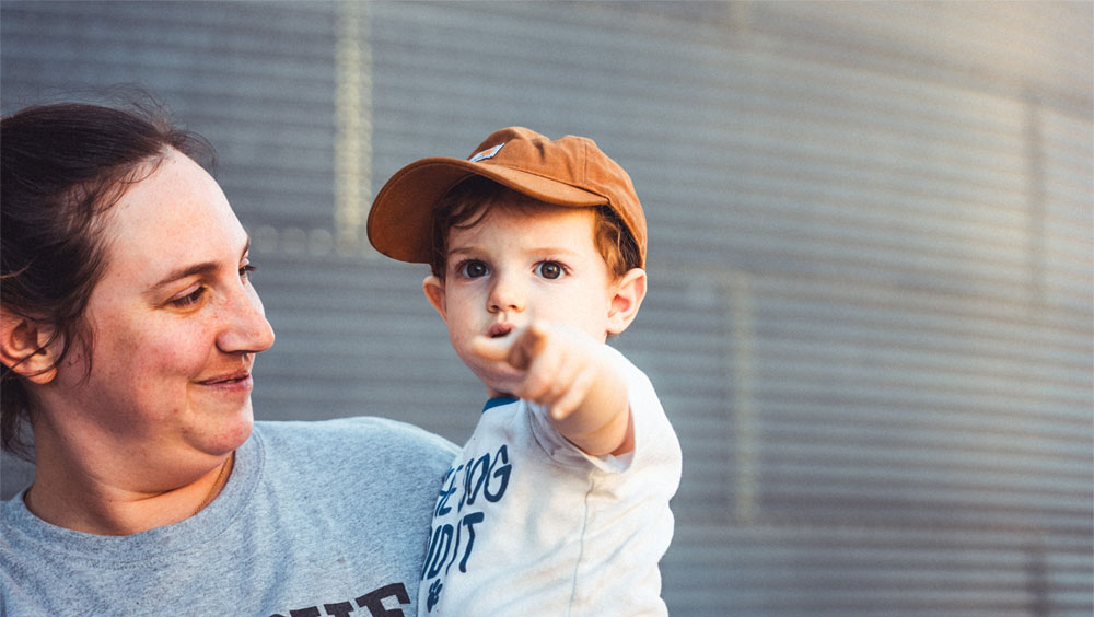 toddler being held by woman and pointing at camera